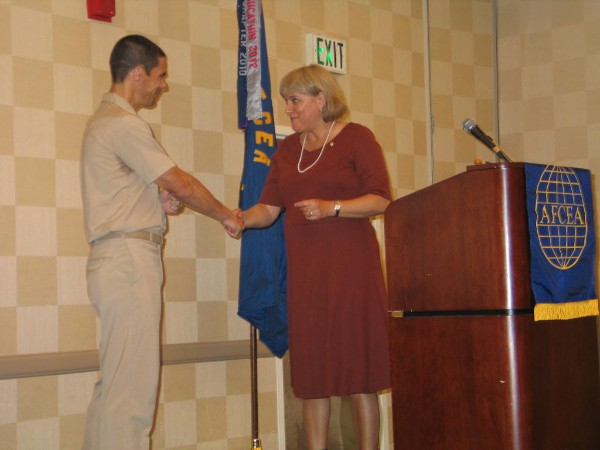 Teresa Duvall, chapter president, extends her gratitude by presenting a chapter coin to Capt. John W. Chandler, USN, commander, Naval Network Warfare Command, as guest speaker at the August monthly luncheon.